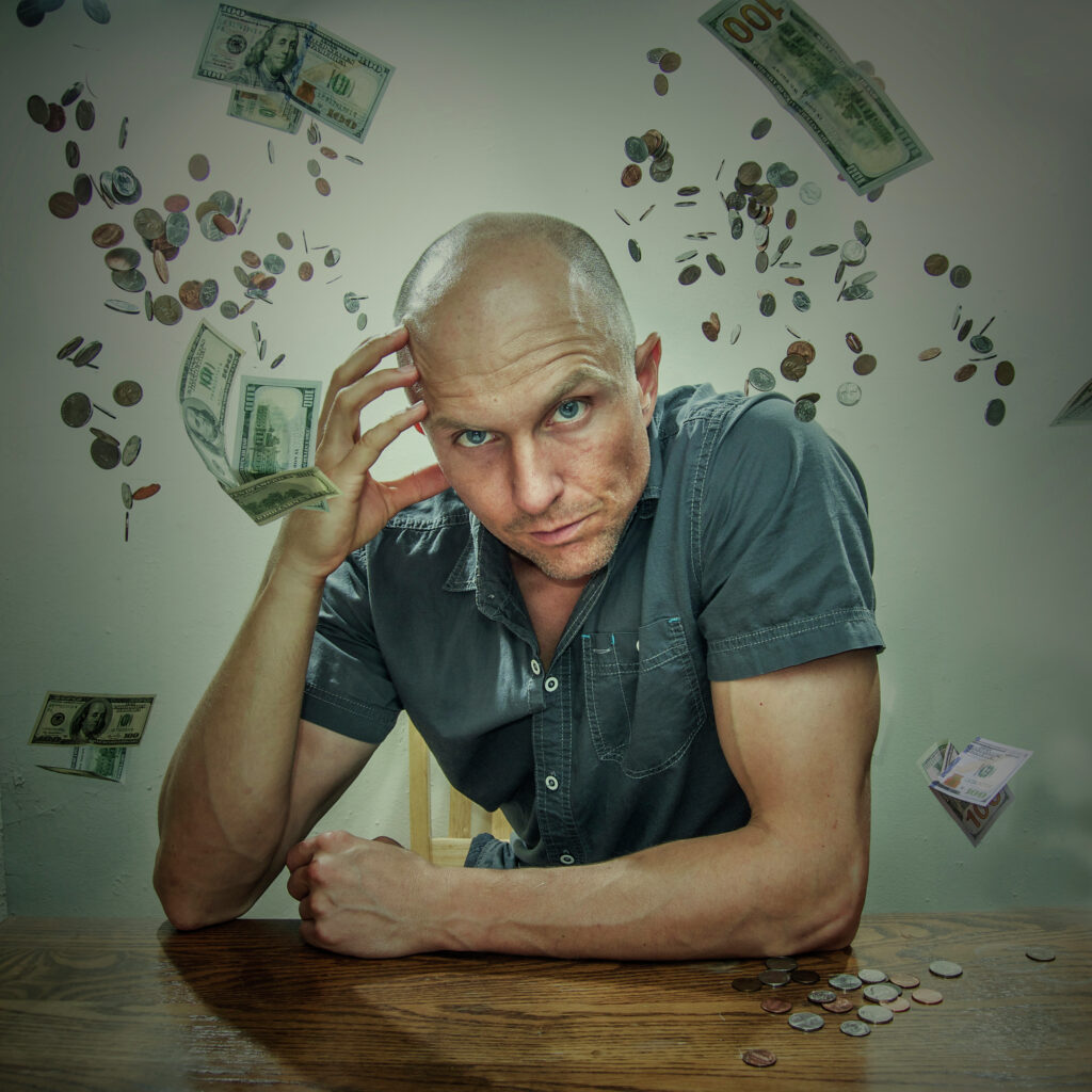 bald-man-in-grey-polo-holding-forehead-and-leaning-forward-on-table-with-cash-and-coin-money-digital-background